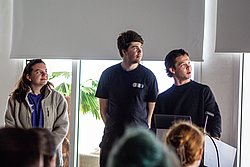 Two men in dark shirts stand in a modern office with plants, looking upward during a presentation or meeting.