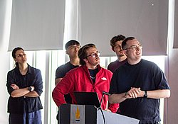 Group of five people standing at a podium with a microphone during a presentation or event