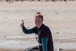 Young surfer in wetsuit giving thumbs up on beach with surfboard