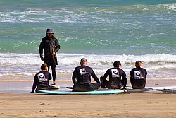 Surfing instructor teaching group of students on beach with surfboards and ocean waves