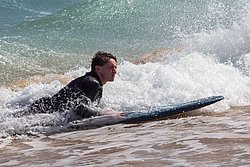 Young surfer in wetsuit riding waves on surfboard in ocean with white foam and turquoise water