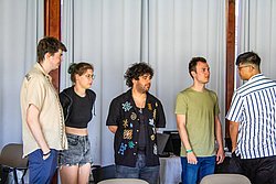 Four young people standing in front of white curtains at an indoor event or presentation